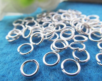 Puede incluir: Un montón de anillos de salto de plata sobre un fondo azul. Los anillos de salto son pequeños y redondos, y son perfectos para la elaboración de joyas.
