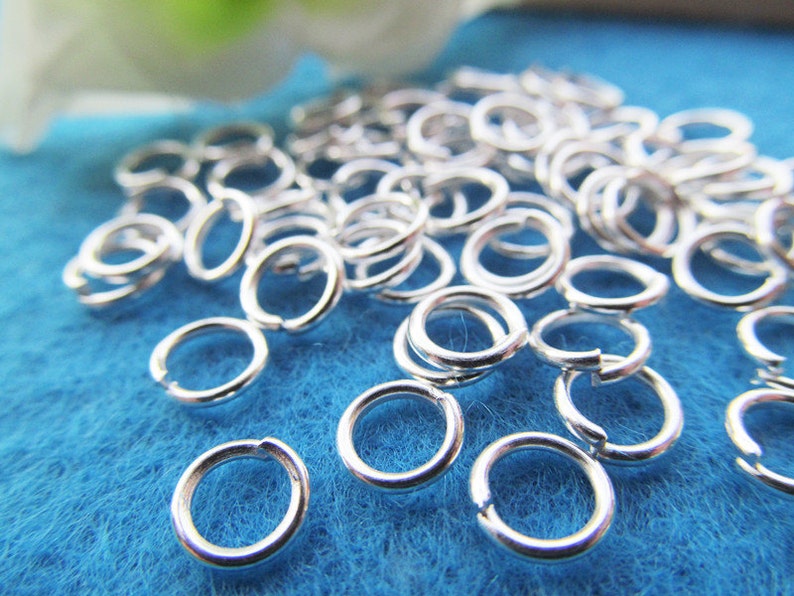 May include: A pile of silver jump rings on a blue background. The jump rings are small and round, and they are perfect for jewelry making.