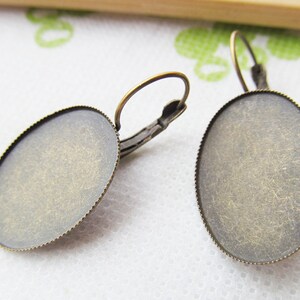 May include: A pair of antique brass oval earring blanks with a scalloped edge. The blanks are ready to be filled with resin, glass, or other materials.