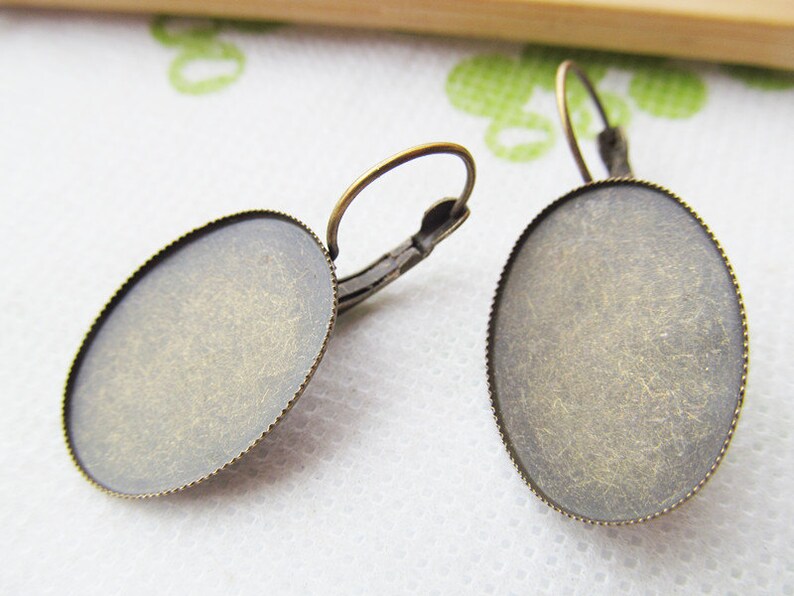 May include: A pair of antique brass oval earring blanks with a scalloped edge. The blanks are ready to be filled with resin, glass, or other materials.