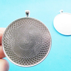 May include: Silver pendant tray with a circular, patterned design. The tray has a loop at the top for hanging.