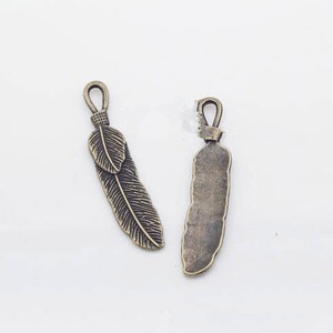 May include: Two antique bronze feather charms with a loop at the top for attaching to jewelry or other crafts.