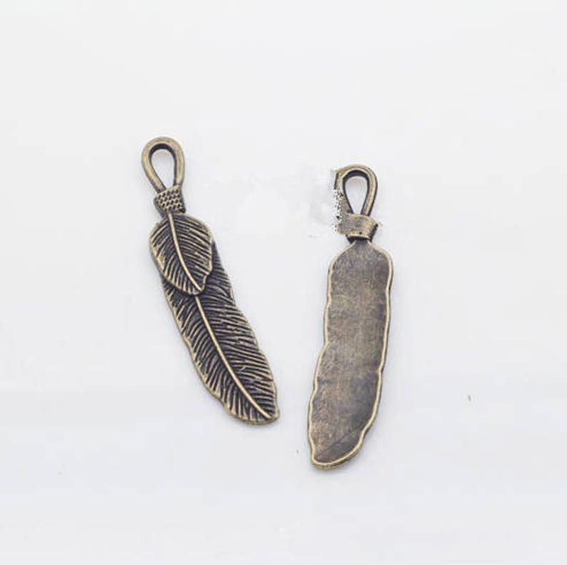 May include: Two antique bronze feather charms with a loop at the top for attaching to jewelry or other crafts.