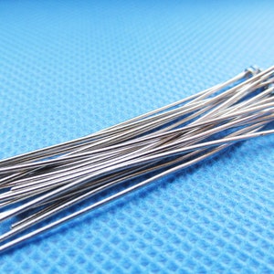 May include: A bundle of silver-colored, straight, thin metal pins with rounded ends. The pins are arranged in a loose pile on a blue textured surface.