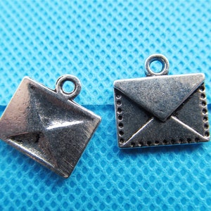 May include: Two silver-toned envelope charms with a loop for hanging. The charms are on a blue background.