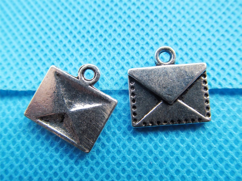 May include: Two silver-toned envelope charms with a loop for hanging. The charms are on a blue background.
