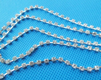 Puede incluir: Borde de cadena de strass plateado con strass transparentes. La cadena es de metal y tiene un acabado brillante.