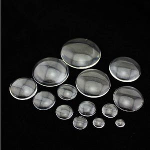 Op de afbeelding: Assortiment van heldere glazen cabochons in verschillende maten. De cabochons zijn rond en hebben een glad, gepolijst oppervlak.