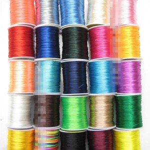 Könnte beinhalten: Sortiment von 24 Spulen mit farbigem elastischem Band, jede auf einer weißen Kunststoffspule gewickelt. Die Bänder sind in verschiedenen Farben, darunter Rot, Blau, Grün, Gelb, Orange, Lila, Rosa, Weiß, Schwarz und Braun.