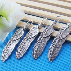 May include: Five silver feather charms with a loop at the top for attaching to jewelry or other crafts. The feathers are detailed with a textured surface and have a slightly oxidized finish.