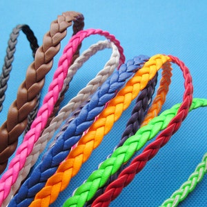 Könnte beinhalten: Eine Sammlung von geflochtenen Kordeln in verschiedenen Farben, darunter Schwarz, Braun, Pink, Weiß, Blau, Orange, Dunkellila, Neongrün und Rot. Jede Kordel weist ein durchgehendes dreisträngiges Flechtmuster aus glattem, flexiblem Material auf.