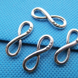 May include: Four silver infinity symbol charms with the word "BFF" engraved on each charm. The charms are on a blue background.
