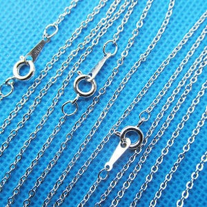Può includere: Un set di collane a catena argentate di diverse lunghezze. Le catene sono tutte realizzate in un metallo fine e delicato e hanno una finitura liscia e lucida.