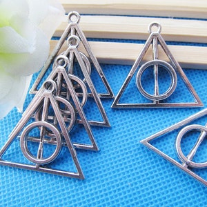 May include: Silver charm pendants in the shape of a triangle with a circle inside. The circle has a line through it. The charms are about 2 inches tall.