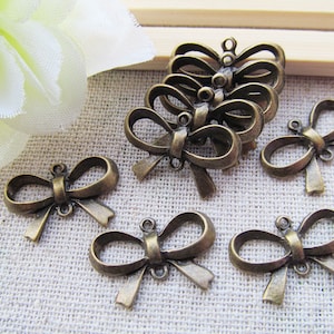 Op de afbeelding: Een set van zeven antieke bronzen strikcharms. De charms zijn in de vorm van een strik met een lus aan de bovenkant om te bevestigen aan een ketting, armband of andere sieraden.