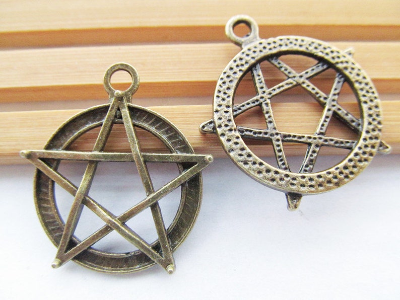 May include: Two antique bronze metal charms in the shape of a five-pointed star. One charm has a solid star design, while the other has a star design with an open center.