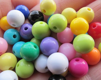 May include: A collection of colorful plastic beads in various shades of green, blue, yellow, pink, purple, and white. The beads are round and have a hole in the center.
