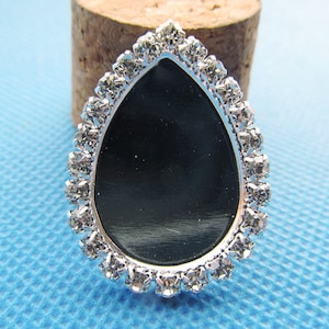 Könnte beinhalten: Ein silberner tropfenförmiger Anhänger mit einem klaren Strasssteinrand und einer schwarzen Mitte.