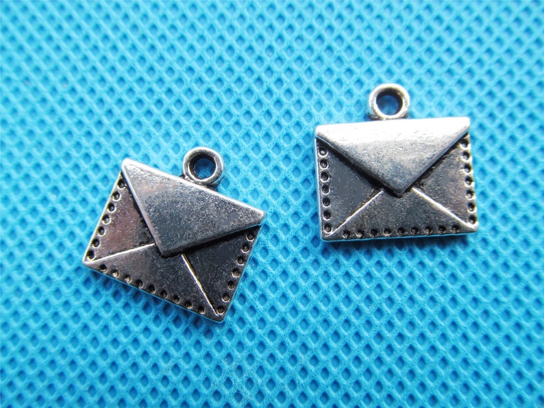 May include: Two silver-toned metal envelope charms with a decorative border. The charms have a loop at the top for attaching to a necklace or bracelet.