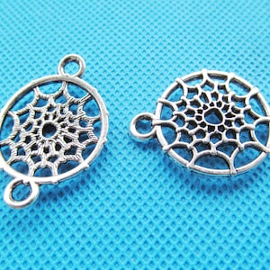 Puede incluir: Dos abalorios de metal plateados en forma de atrapasueños con diseños intrincados. Cada abalorio es circular con un patrón de telaraña y tres bucles para sujetar a joyas u otras manualidades.