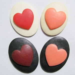 May include: Four oval-shaped heart-shaped buttons. Two buttons are white with a red heart and a pink heart. The other two buttons are black with a maroon heart and a pink heart.