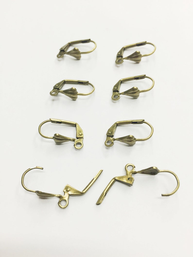 May include: A set of eight gold-toned earring hooks. The hooks are made of metal and have a teardrop-shaped design. The hooks are designed to be used with earrings.