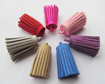 May include: Assortment of eight suede tassels in various colours, including grey, beige, blue, purple, pink, and red. The tassels are arranged in a circle on a white background.