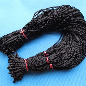 Puede incluir: Un paquete de cordón trenzado negro, atado con cuerda roja. El cordón tiene aproximadamente 3 mm de grosor.