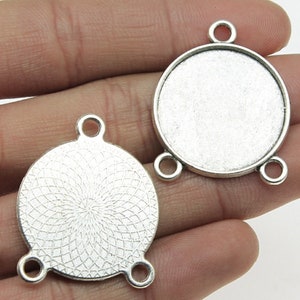 Op de afbeelding: Twee zilverkleurige metalen hangerbedels met drie springringen. Een bedel heeft een glad, rond oppervlak, terwijl de andere een decoratief, cirkelvormig patroon heeft.
