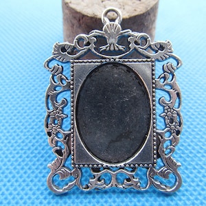Może przedstawiać: Srebrny wisiorek z metalu z ozdobną ramką i czarnym owalnym kameą. Ramka ma ozdobny wzór z motywami kwiatowymi.