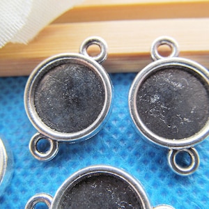 May include: Four silver-toned metal pendant trays with a round bezel and three loops. The trays are designed to hold round cabochons or other embellishments.