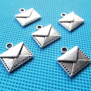 May include: Five silver-toned envelope charms with a detailed design. The charms have a loop at the top for attaching to jewelry or other crafts.