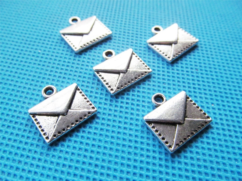 May include: Five silver-toned envelope charms with a detailed design. The charms have a loop at the top for attaching to jewelry or other crafts.