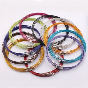 May include: A collection of 18 thin, colorful metal necklaces. The necklaces are arranged in a circle, with the ends of each necklace overlapping. The necklaces are made of a variety of colors, including red, orange, yellow, green, blue, purple, and silver.