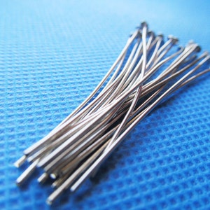 May include: A bundle of silver-colored straight pins on a blue textured surface.