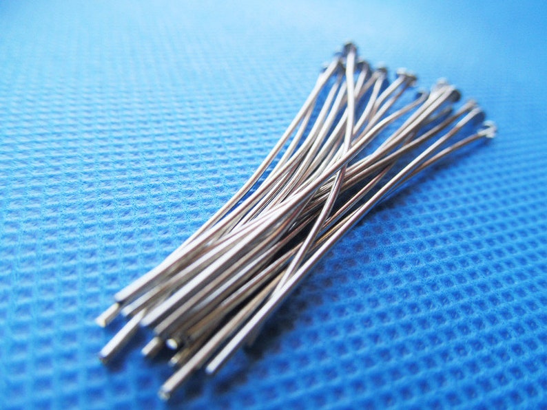 May include: A bundle of silver-colored straight pins on a blue textured surface.