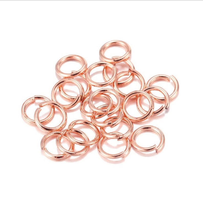 May include: A pile of rose gold jump rings, a type of jewelry finding used for connecting chains, cords, and other jewelry components.