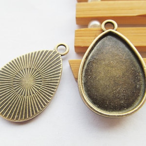 Könnte beinhalten: Zwei antike goldfarbene Metall-Anhänger in Tropfenform. Ein Anhänger hat eine glatte Oberfläche, während der andere ein strukturiertes, radiales Muster aufweist.