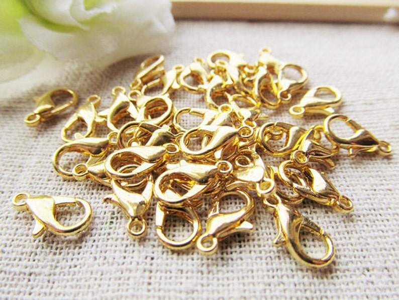 Puede incluir: Un mont&oacute;n de cierres de langosta de metal dorado, com&uacute;nmente utilizados para la fabricaci&oacute;n de joyas.