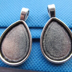 Op de afbeelding: Twee zilverkleurige hangerbevestigingen in een druppelvorm. De bevestigingen zijn ontworpen om een cabochonsteen te houden.