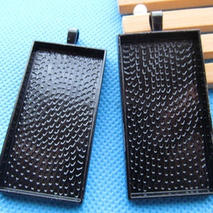 Peut inclure: Deux plateaux rectangulaires en métal noir pour pendentif avec une surface texturée. Les plateaux ont une boucle en haut pour accrocher.