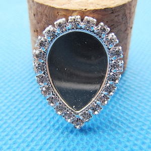 Könnte beinhalten: Ein silberner tropfenförmiger Anhänger mit einer klaren Glasmitte, umgeben von einem Rand aus klaren Strasssteinen.