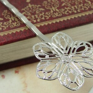 May include: Silver hair clip with a delicate flower design. The flower has a filigree pattern and is made of metal.