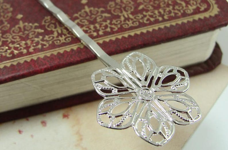 May include: Silver hair clip with a delicate flower design. The flower has a filigree pattern and is made of metal.