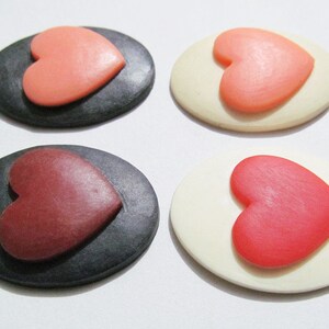 May include: Four oval-shaped decorative pieces with a heart design. Two pieces are black with a pink heart, and two pieces are white with a red heart.
