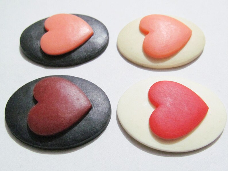 May include: Four oval-shaped decorative pieces with a heart design. Two pieces are black with a pink heart, and two pieces are white with a red heart.