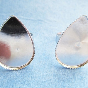 Könnte beinhalten: Zwei silberne ringrohlinge in Tropfenform mit einem gewellten Rand. Die Rohlinge sind bereit, mit Harz oder anderen Materialien gefüllt zu werden.