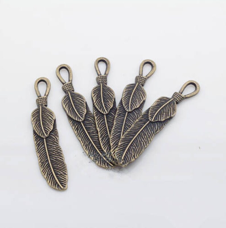 May include: Five antique bronze feather charms with a loop at the top for attaching to jewelry or other crafts.