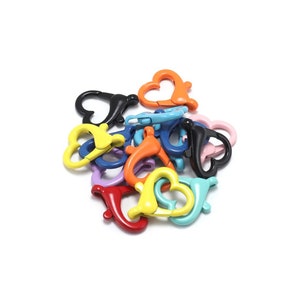 May include: Assortment of colourful heart-shaped metal clasps. The clasps are in various colours, including red, orange, yellow, green, blue, purple, and black.