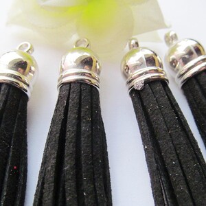 May include: Four black suede tassels with silver metal caps. The tassels are approximately 2 inches long.